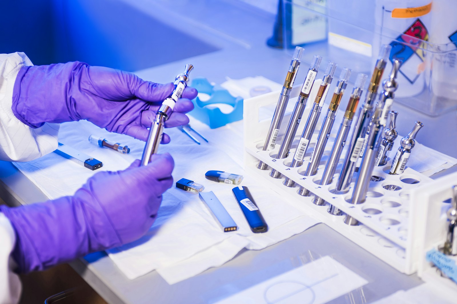 A person in purple gloves inspecting a vape pen in a laboratory setting