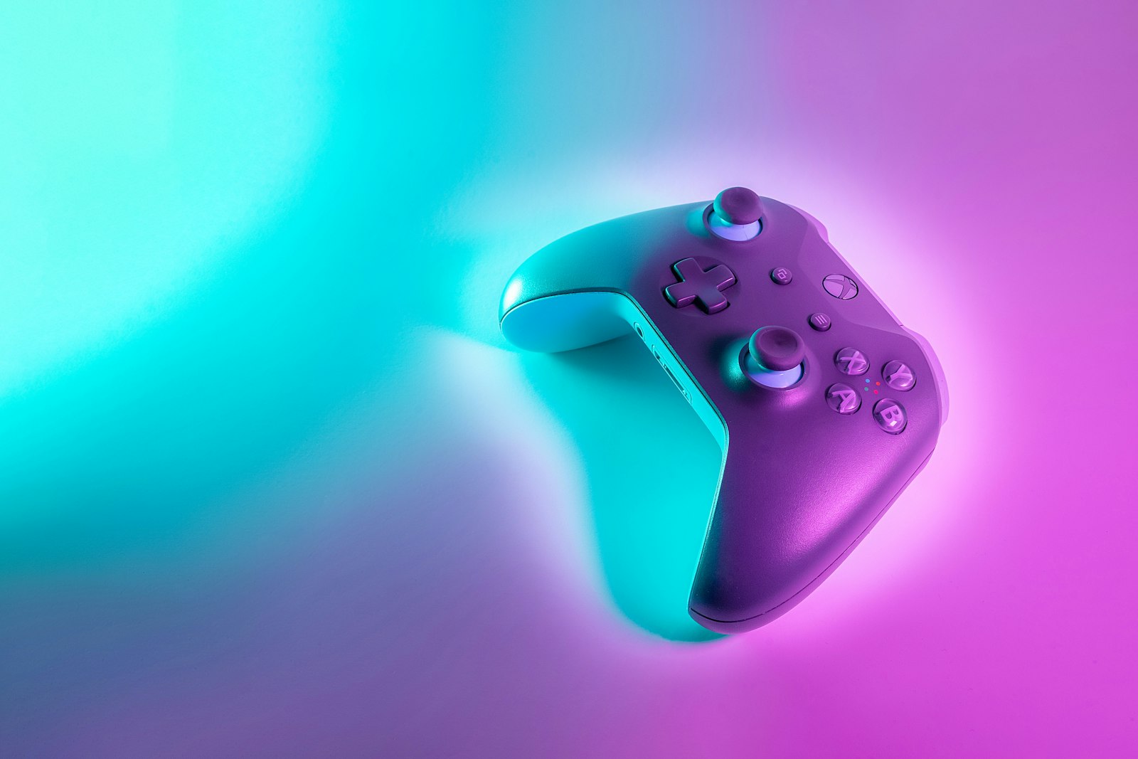 A wireless game controller illuminated by vibrant cyan and magenta neon light