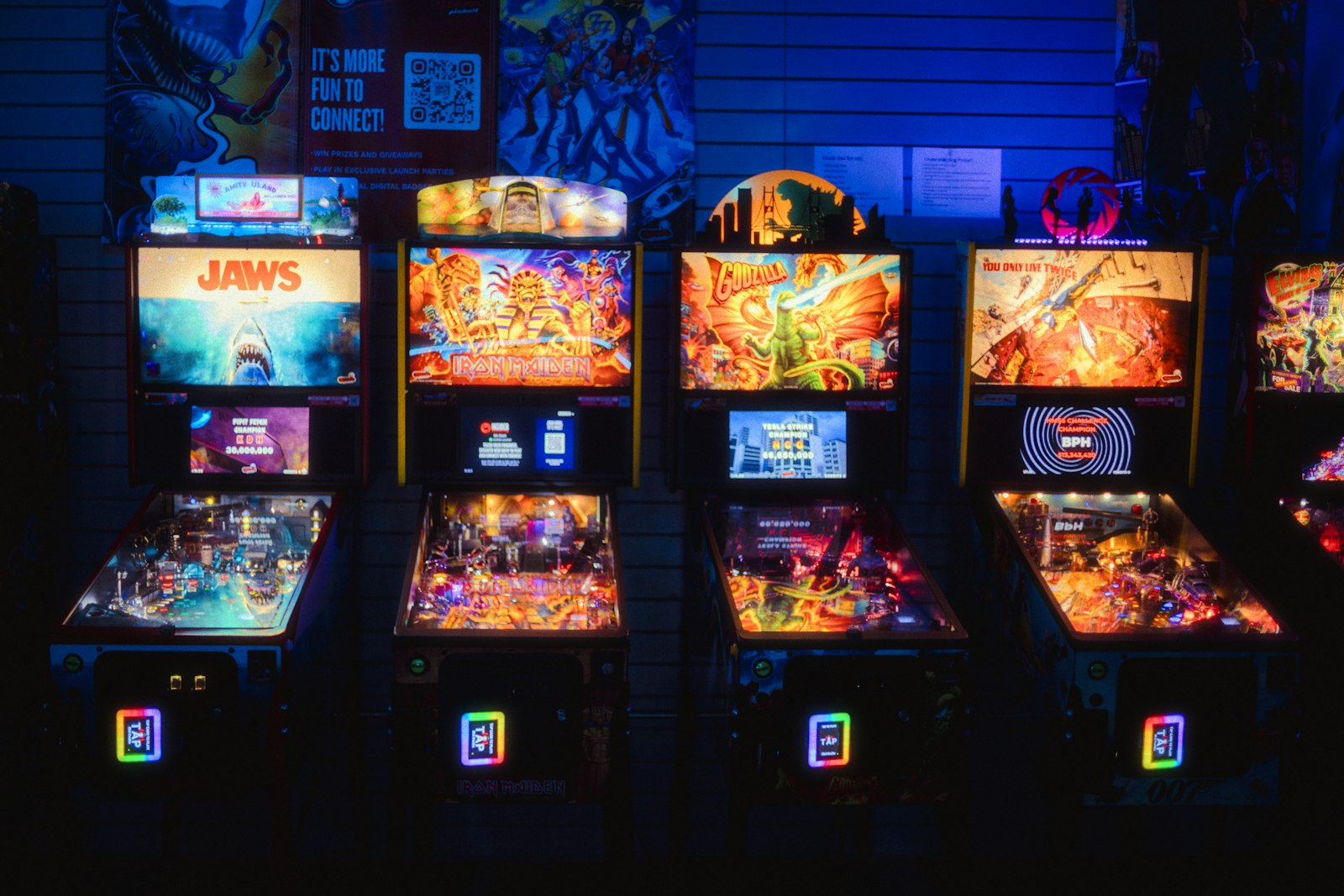 Several illuminated pinball machines in a dark arcade.