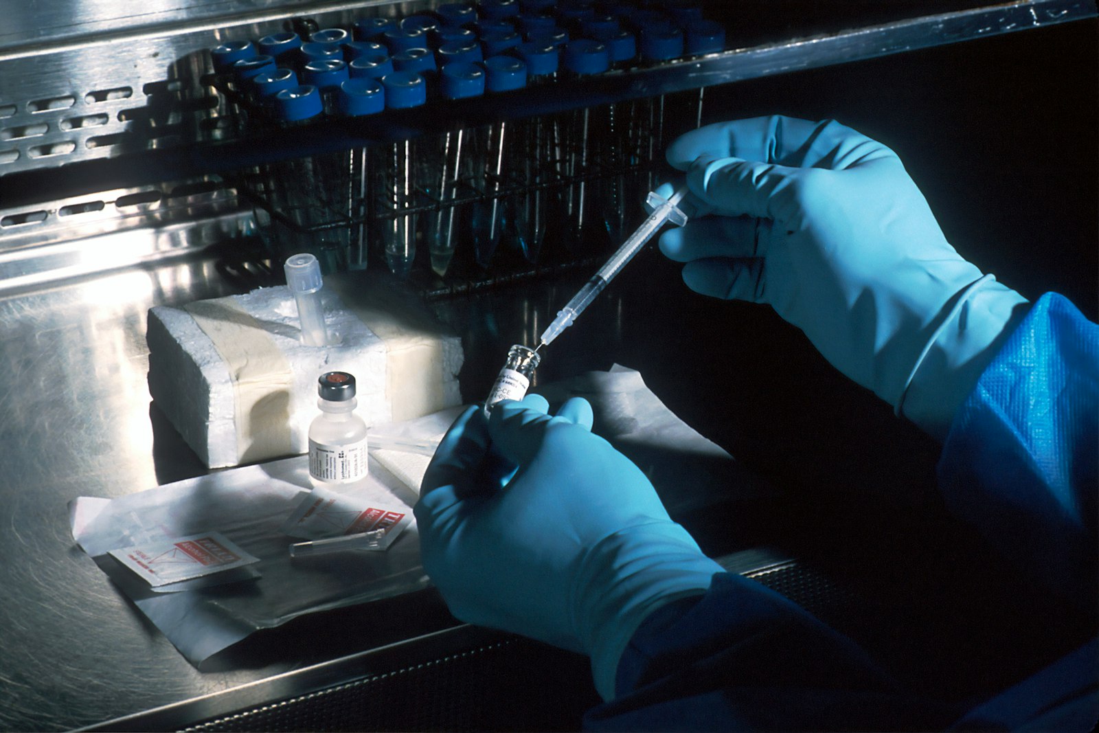 Gloved hands drawing vaccine from vial with syringe