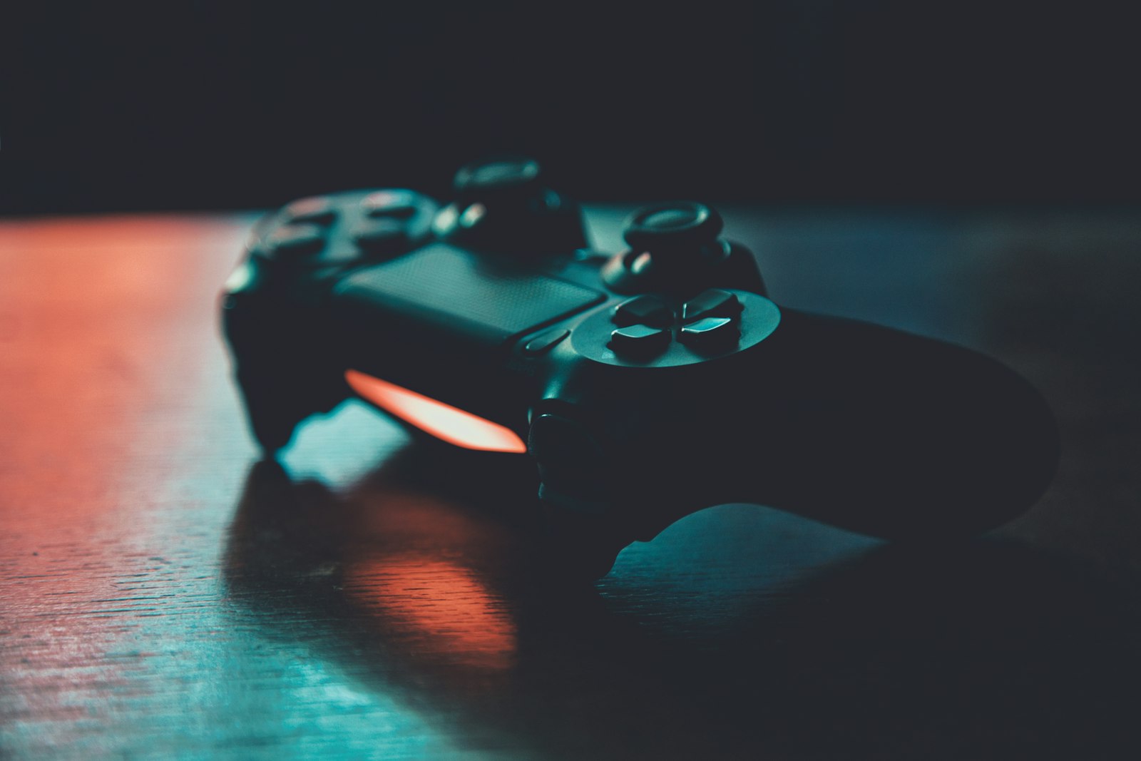 A black game controller on a wooden surface with blue and orange lighting